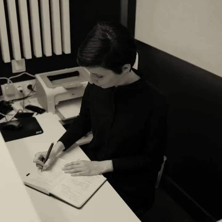 Profissional escreve num caderno, à mesa de um escritório
