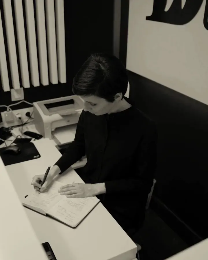 Profissional escreve num caderno, à mesa de um escritório