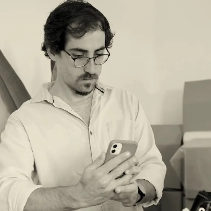Lojista de óculos confere o celular ao lado de uma caixa de encomenda